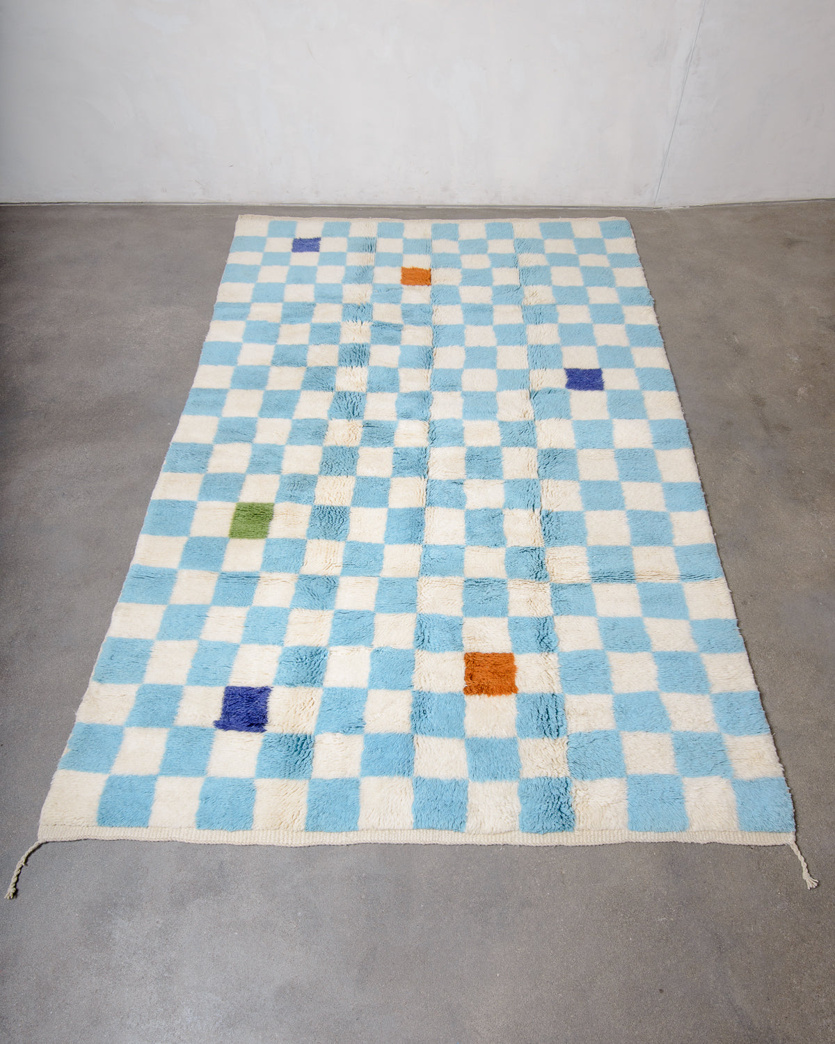 Berberlin Beni M'rirt wool rug in cream and light blue checkerboard design, laying flat on a concrete floor. Five of the checkered squares are a different colour.